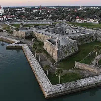 An aerial view of Castillo de San Marcos in St. Augustine, Florida, by the water with a city skyline in the background.