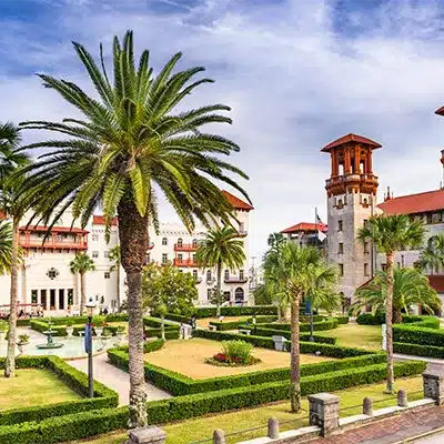 A palm-lined courtyard with manicured hedges and a historic building with a tower in St. Augustine, Florida.