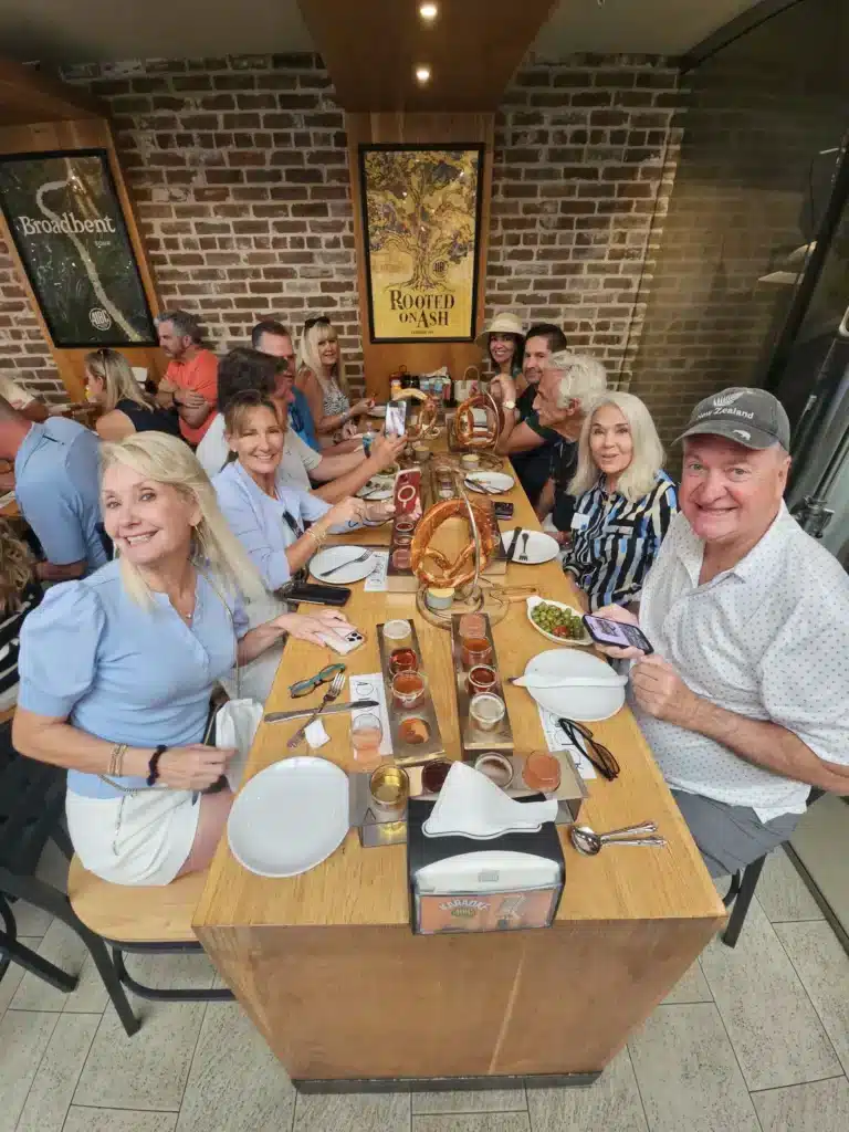 A group of people sit around a long wooden table in a restaurant with brick walls, smiling at the camera.