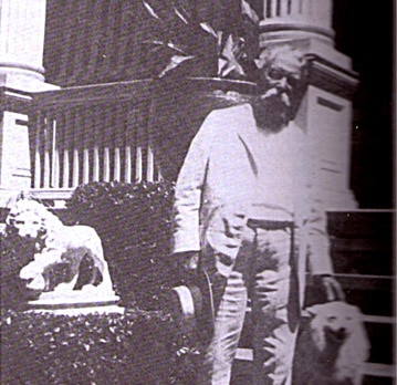 A black and white photograph of Mark Twain standing outside with a statue of a lion and a small dog.