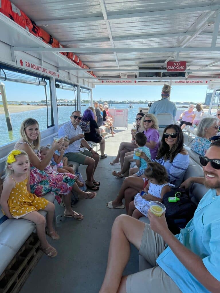 People sit on both sides of a boat deck, facing forward toward the water under a canopy.