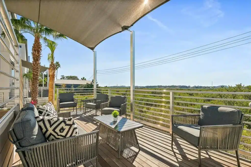 A sunny outdoor deck with a shaded seating area, patio furniture, and views of a green landscape.