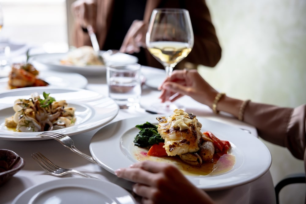 People dining at a restaurant table with plates of food, cutlery, and wine glasses.