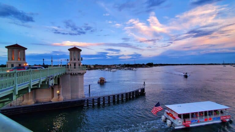A boat with an American flag travels under the Bridge of Lions in St. Augustine at twilight.